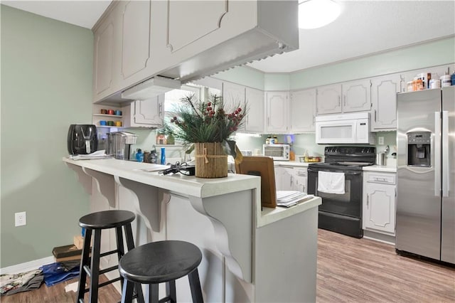 kitchen with black electric range oven, a breakfast bar area, a peninsula, white microwave, and stainless steel refrigerator with ice dispenser