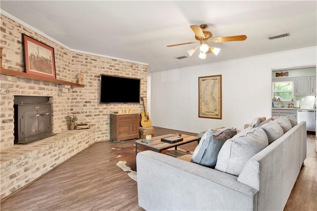 living room with ornamental molding, wood finished floors, visible vents, and ceiling fan