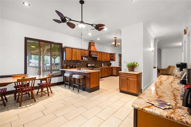 kitchen featuring a breakfast bar, custom exhaust hood, crown molding, ceiling fan with notable chandelier, and backsplash