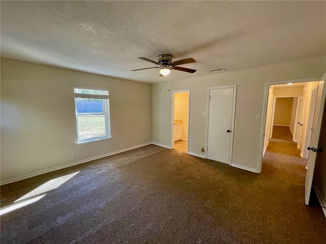 unfurnished bedroom with ceiling fan, a textured ceiling, dark carpet, a closet, and ensuite bath