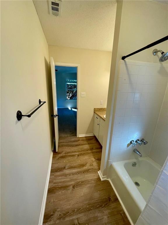 bathroom featuring vanity, bathtub / shower combination, a textured ceiling, wood finished floors, and visible vents