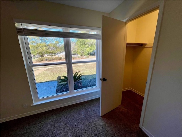 unfurnished bedroom featuring dark carpet, baseboards, a spacious closet, and a closet