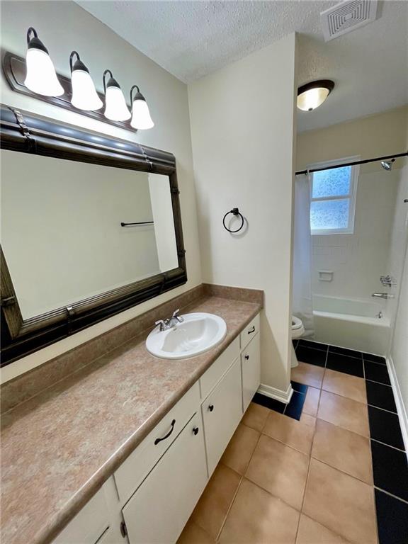 full bathroom with a textured ceiling, toilet, vanity, washtub / shower combination, and tile patterned flooring