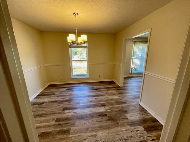 unfurnished dining area with a notable chandelier, a textured ceiling, and dark hardwood / wood-style floors