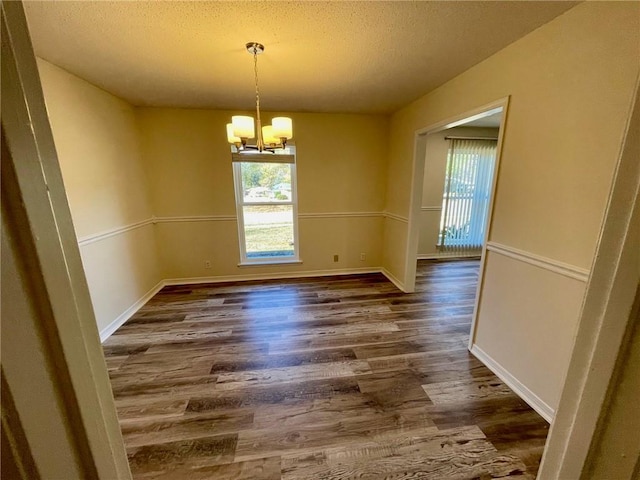 unfurnished dining area with a healthy amount of sunlight, dark wood-style floors, a textured ceiling, and a chandelier