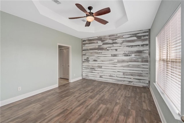 spare room featuring dark wood-type flooring, ceiling fan, a raised ceiling, and wood walls