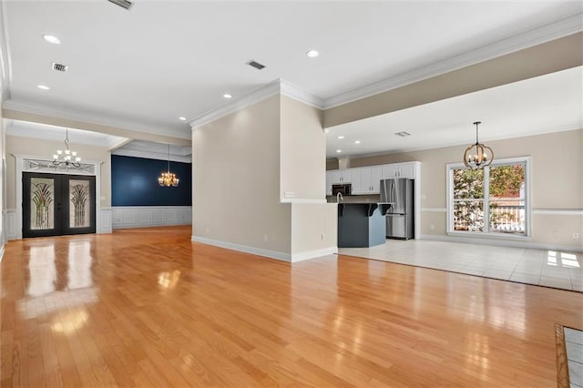 unfurnished living room featuring crown molding, an inviting chandelier, and light hardwood / wood-style floors