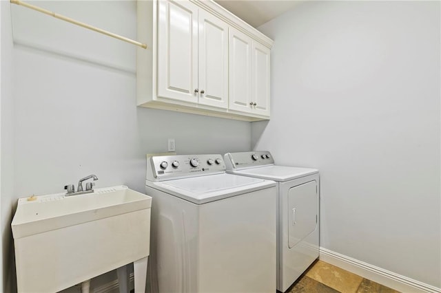 clothes washing area with washer and clothes dryer, sink, and cabinets