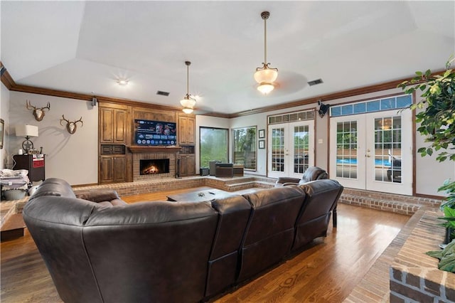 living room with wood-type flooring, crown molding, a tray ceiling, and french doors