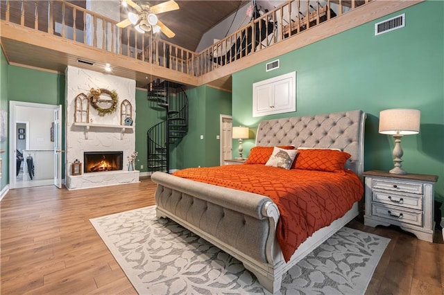 bedroom with ceiling fan, wooden ceiling, hardwood / wood-style floors, a towering ceiling, and a fireplace