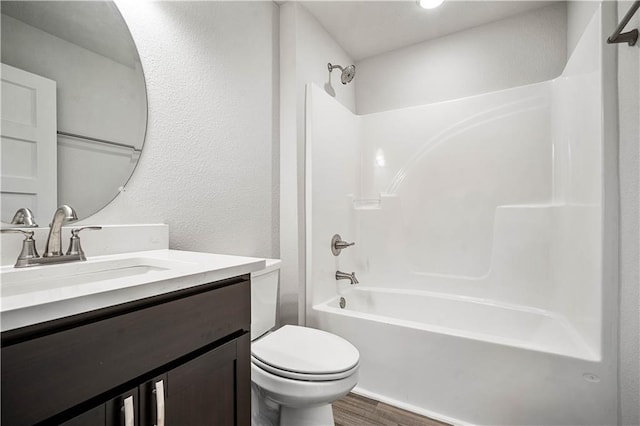 bathroom featuring a textured wall, toilet, wood finished floors, vanity, and shower / washtub combination