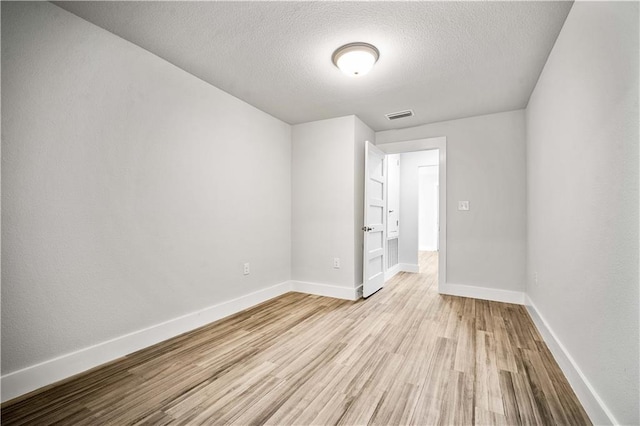 spare room featuring light wood-type flooring, baseboards, visible vents, and a textured ceiling