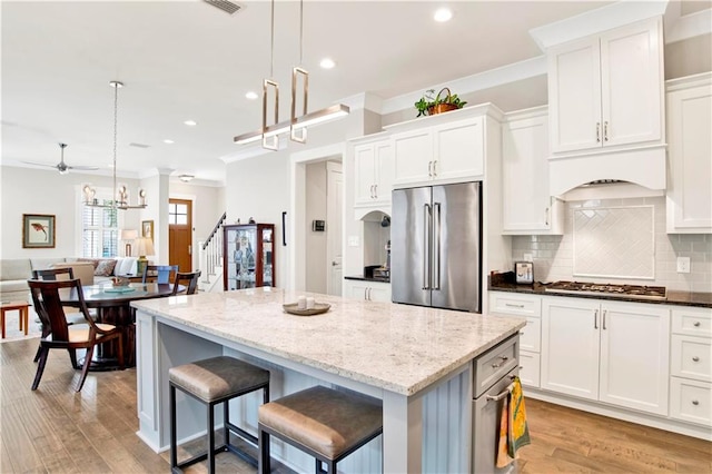 kitchen with appliances with stainless steel finishes, light hardwood / wood-style flooring, a kitchen island, and hanging light fixtures