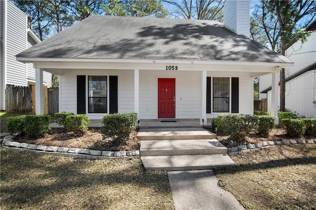 view of front facade with a chimney, a porch, a shingled roof, and fence