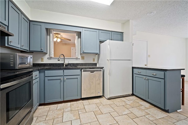 kitchen featuring a sink, ceiling fan, stainless steel appliances, a textured ceiling, and dark countertops