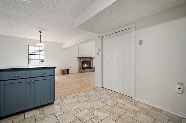 kitchen with blue cabinets, a textured ceiling, a brick fireplace, decorative light fixtures, and open floor plan