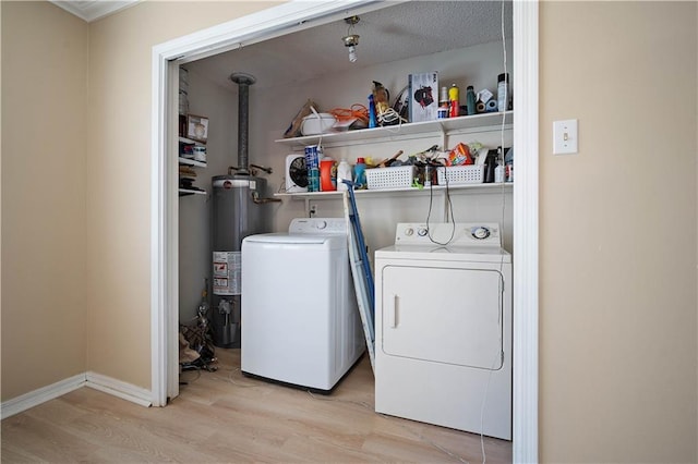 washroom featuring water heater, light wood-style floors, baseboards, laundry area, and washing machine and clothes dryer