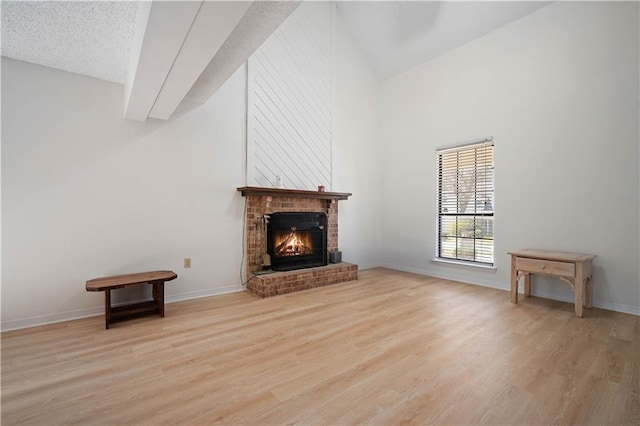 unfurnished living room featuring light wood-style flooring, a brick fireplace, high vaulted ceiling, and baseboards