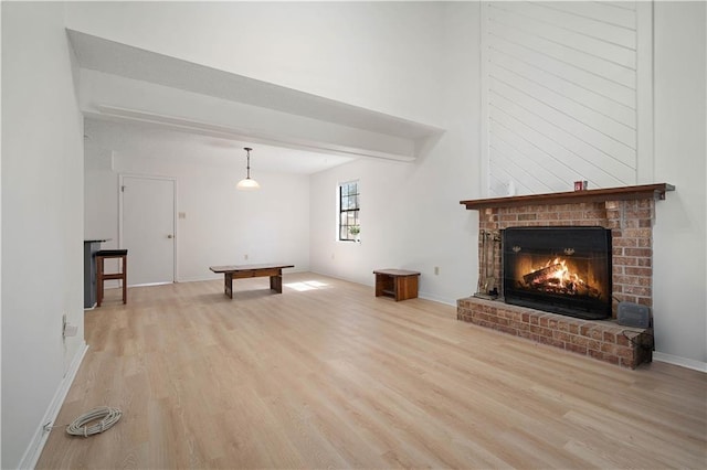 unfurnished living room with a fireplace, beam ceiling, wood finished floors, and baseboards