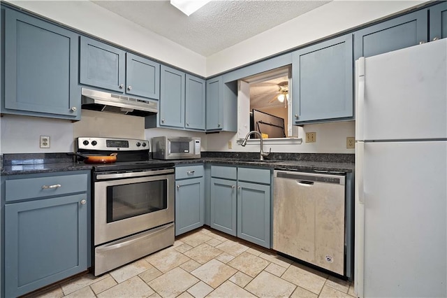 kitchen with blue cabinets, under cabinet range hood, a sink, a textured ceiling, and appliances with stainless steel finishes