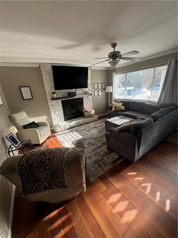 living room with hardwood / wood-style floors, ceiling fan, a stone fireplace, and crown molding