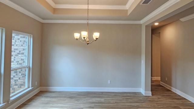 spare room featuring an inviting chandelier, a tray ceiling, ornamental molding, and hardwood / wood-style flooring