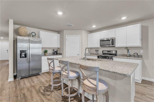 kitchen featuring stainless steel appliances, visible vents, a sink, an island with sink, and light wood-type flooring