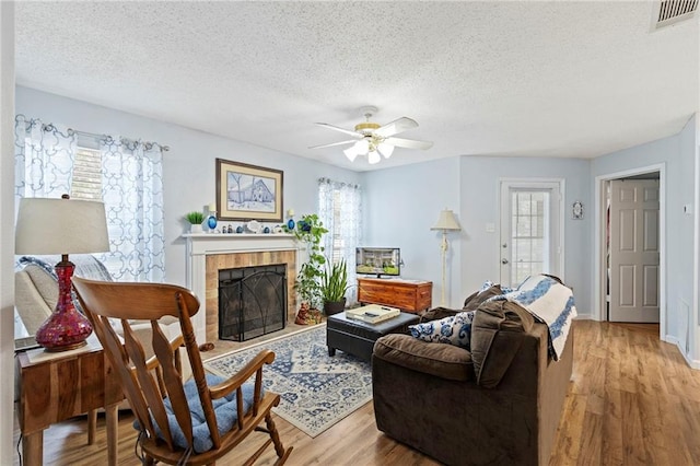 living room featuring light wood-style flooring, a ceiling fan, visible vents, and a wealth of natural light