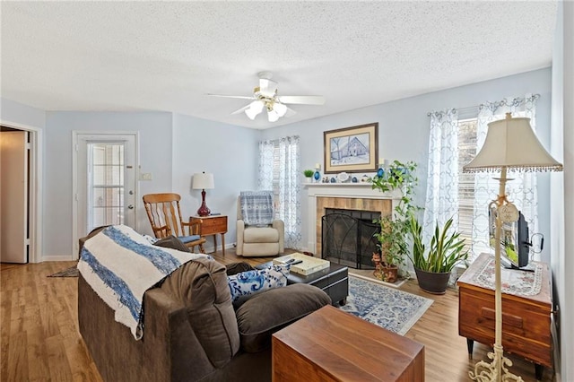 living area featuring light wood-type flooring, a textured ceiling, ceiling fan, and a fireplace