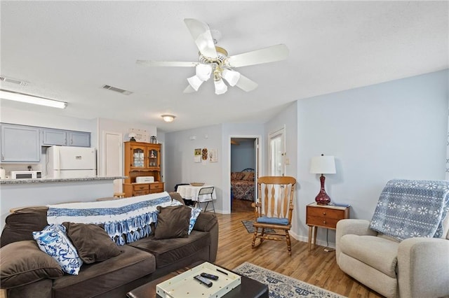 living room with light wood finished floors, visible vents, baseboards, and ceiling fan