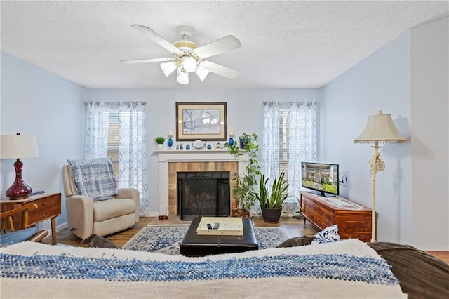 living room with a ceiling fan, a textured ceiling, wood finished floors, and a fireplace