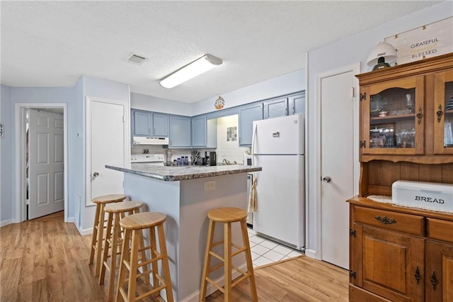 kitchen with visible vents, light wood-style flooring, freestanding refrigerator, under cabinet range hood, and a kitchen breakfast bar