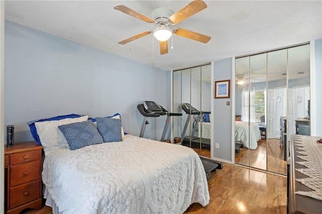 bedroom with a textured ceiling, wood finished floors, multiple closets, and ceiling fan