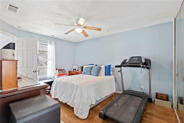 bedroom featuring ceiling fan, wood finished floors, visible vents, and a textured ceiling