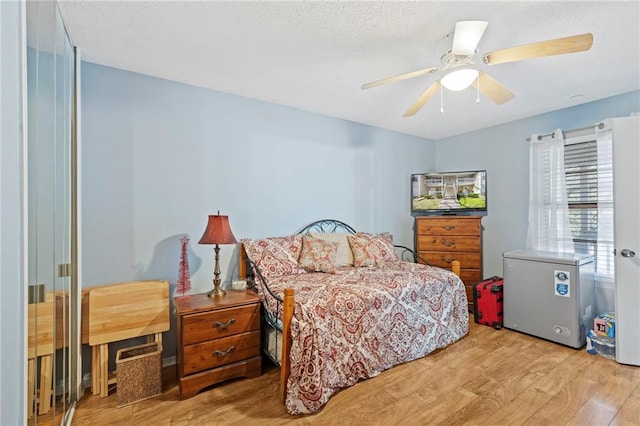 bedroom with a textured ceiling, fridge, wood finished floors, and ceiling fan