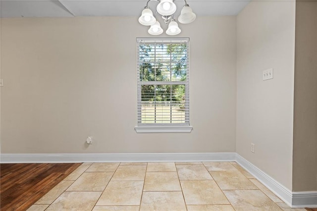 empty room featuring a healthy amount of sunlight, a notable chandelier, and light wood-type flooring