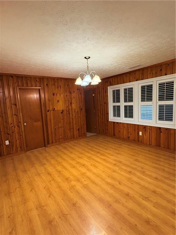 spare room featuring an inviting chandelier, light hardwood / wood-style flooring, and a textured ceiling