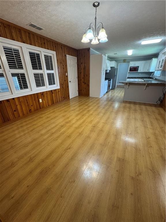 unfurnished living room with a chandelier, light hardwood / wood-style flooring, wooden walls, and a textured ceiling