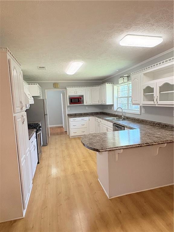 kitchen with gas range, kitchen peninsula, sink, and white cabinets