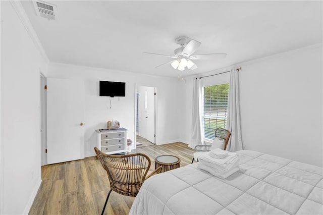 bedroom with baseboards, visible vents, wood finished floors, ceiling fan, and crown molding