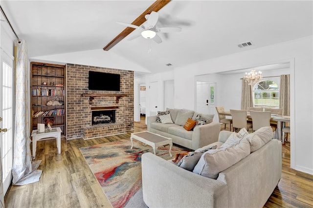 living area featuring wood finished floors, visible vents, lofted ceiling with beams, a fireplace, and ceiling fan with notable chandelier