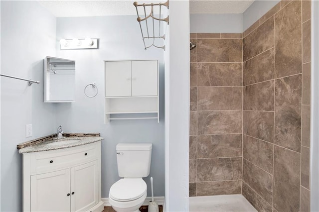 full bath featuring toilet, vanity, tiled shower, and a textured ceiling