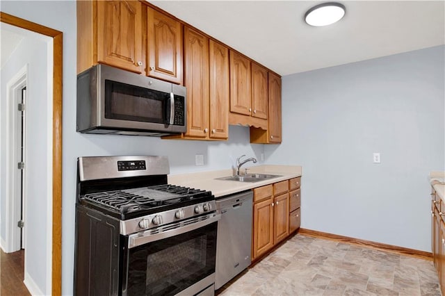 kitchen featuring light countertops, a sink, brown cabinetry, stainless steel appliances, and baseboards