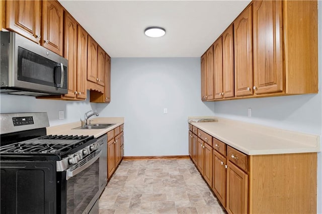 kitchen featuring light countertops, stone finish floor, baseboards, appliances with stainless steel finishes, and a sink
