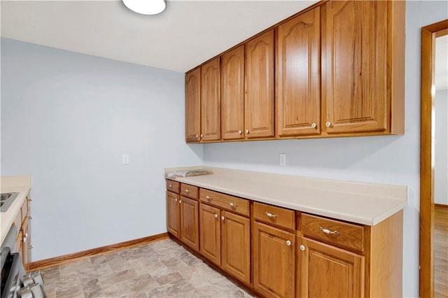 kitchen featuring light countertops, baseboards, and brown cabinetry