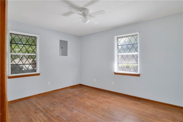 empty room featuring a textured ceiling, electric panel, baseboards, wood finished floors, and a ceiling fan