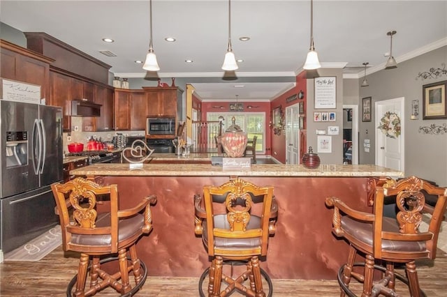 kitchen featuring a breakfast bar area, stainless steel appliances, wood finished floors, and pendant lighting