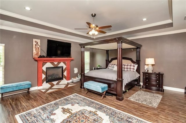 bedroom with wood finished floors, baseboards, ornamental molding, a tray ceiling, and a tiled fireplace