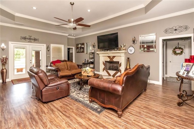 living room with a tray ceiling, french doors, ornamental molding, wood finished floors, and a tile fireplace