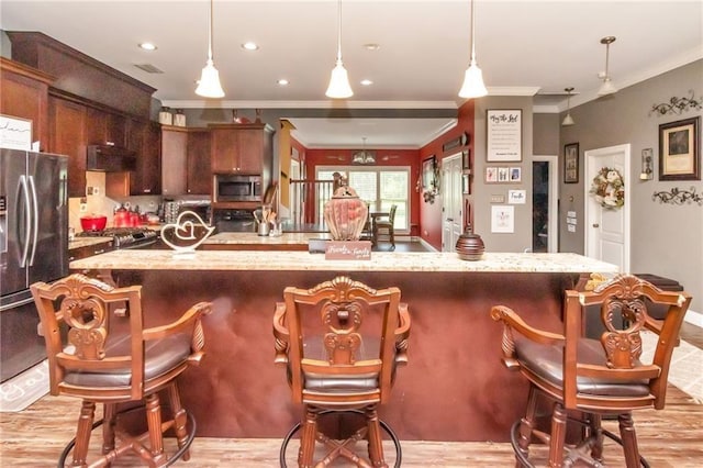 kitchen featuring a kitchen breakfast bar, light wood-style floors, appliances with stainless steel finishes, decorative light fixtures, and crown molding